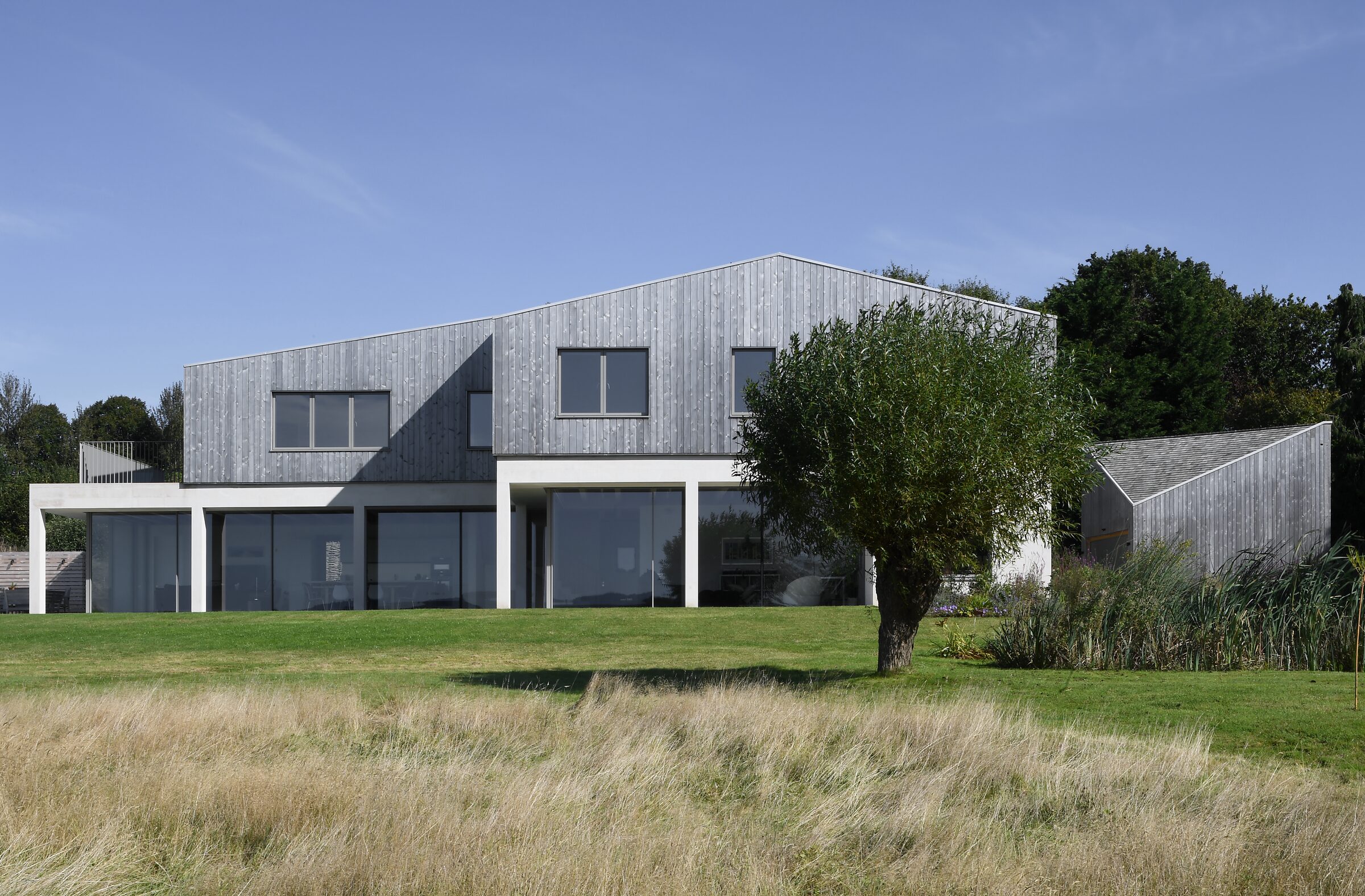 Field House, a timber-clad home with a sawtooth roofline set in a wildflower meadow
