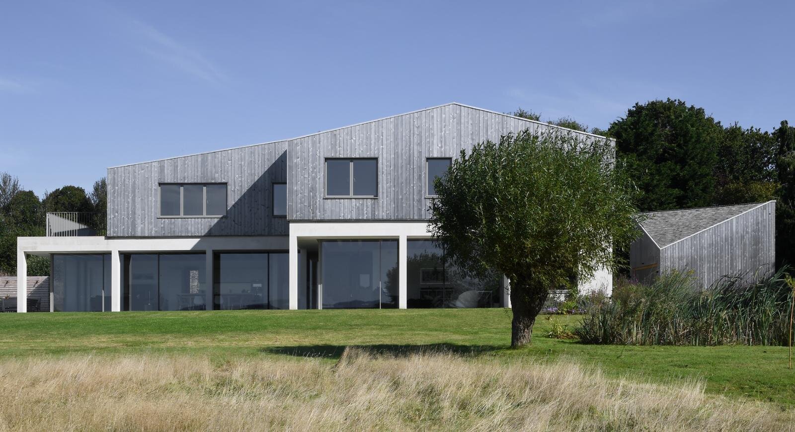 Field House, a timber-clad home with a sawtooth roofline set in a wildflower meadow